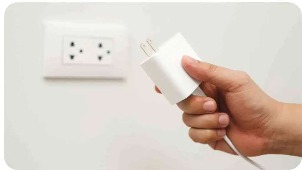 a hand is holding a white plug in front of a wall outlet